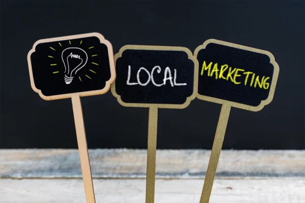 Three small wood label tags that have a lightbulb drawn on one, the word local on another, and marketing on the third